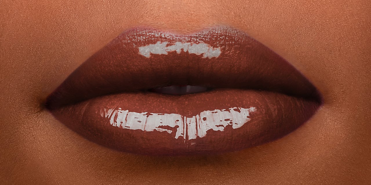 Dark chocolate brown lip gloss in an 80s shade worn on a model with dark skin